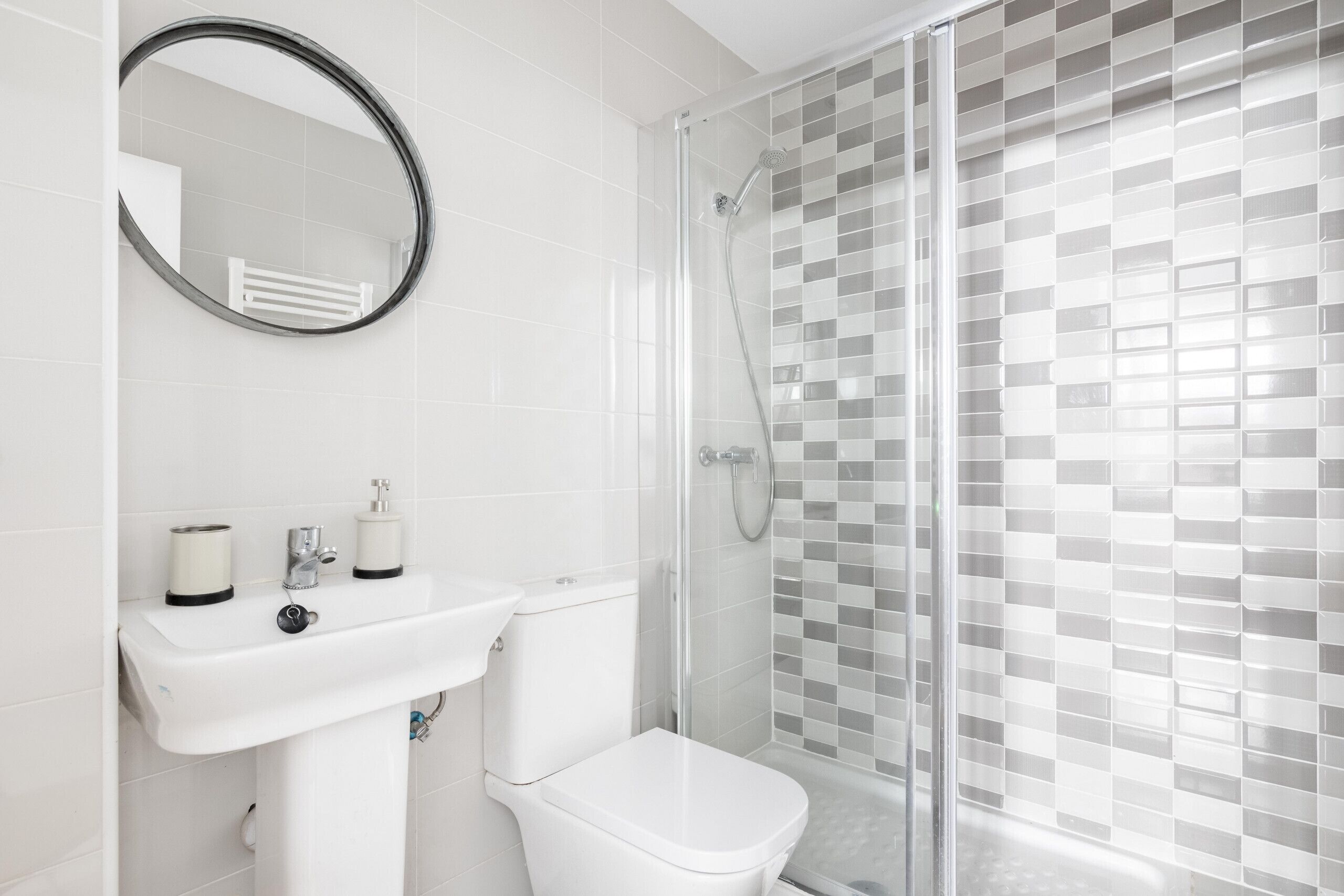 Un baño moderno con lavamanos blanco, inodoro y cabina de ducha con mampara de vidrio.