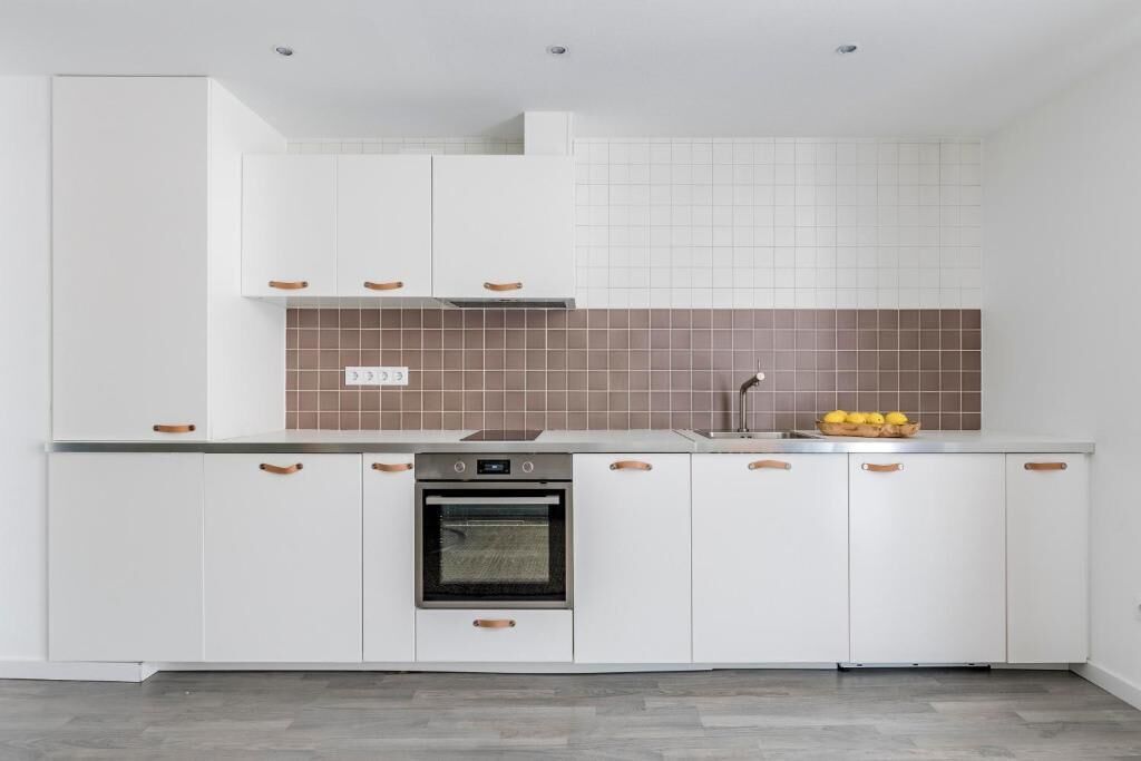 A modern kitchen with white cabinets, a brown backsplash, and a built-in oven.