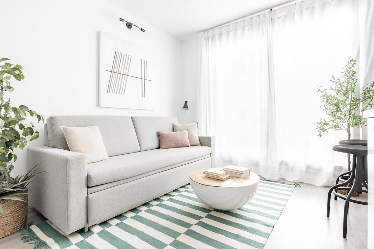 Una sala moderna con un sofá gris, una mesa redonda de centro y un tapete a rayas.