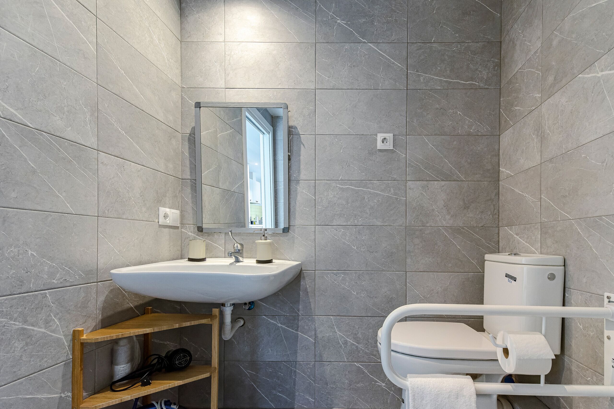 Un baño moderno con lavamanos, espejo y inodoro blancos.