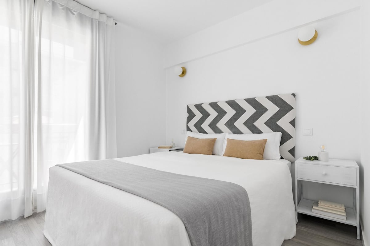 Un dormitorio moderno con una cama grande, paredes blancas, un cabecero estampado en patrón chevron y una mesita de noche con lámpara.