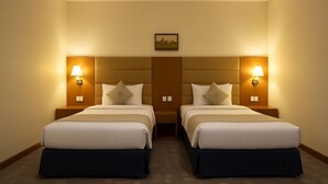 A hotel room with two beds, each with a headboard, bedside lamps, and a small painting above the headboard. - Tamr Inn Hotel (Dubai)