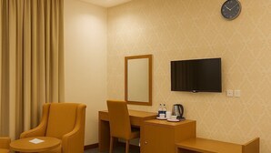 A hotel room with a desk, two chairs, a television, and a clock on the wall. - Tamr Inn Hotel (Dubai)