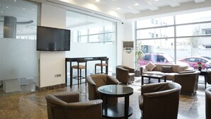 A modern lobby with seating areas, a flat-screen TV, and large windows offering views of parked cars and buildings. - Tamr Inn Hotel (Dubai)