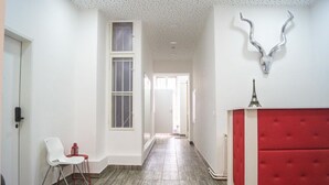 Un pasillo con un banco tapizado en rojo, una silla blanca y una cornamenta decorativa en la pared.