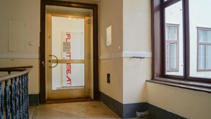 Un pasillo con una puerta que indica 'FLAT TIME AT', una ventana y un cubo de basura pequeño.