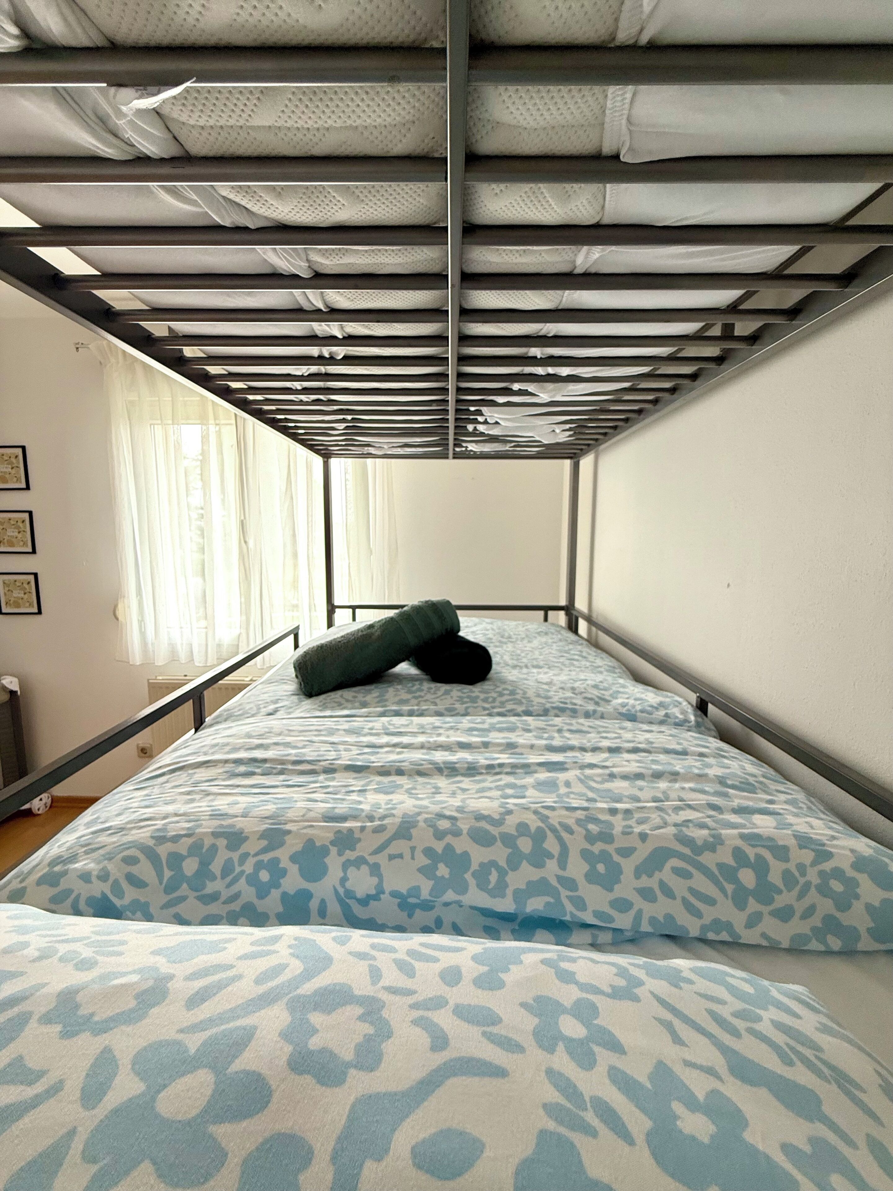 A small, single-bed room with a metal frame, a patterned bedspread, and a pillow.