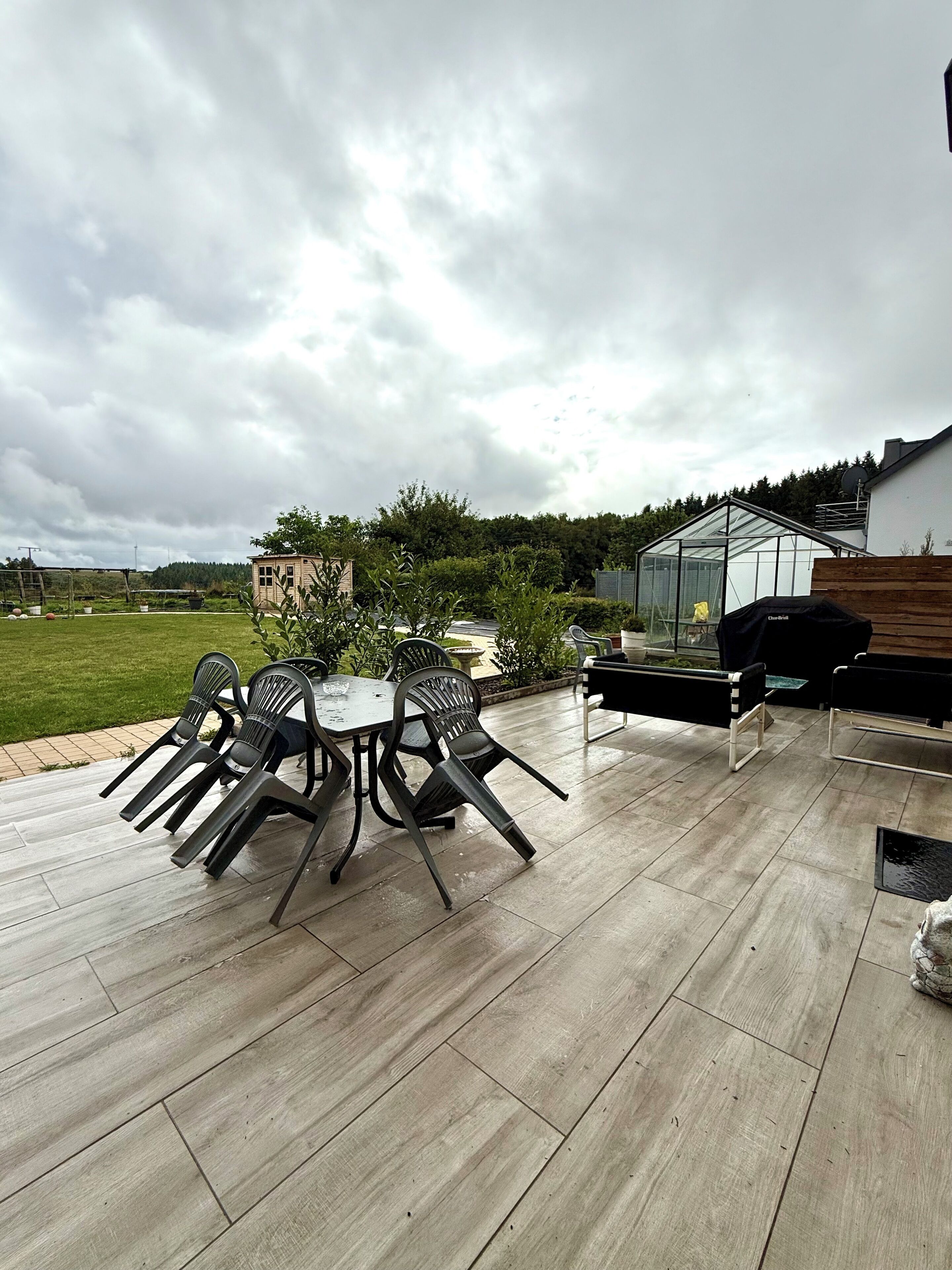 An outdoor patio with a table and chairs, a greenhouse, and a wooden deck.