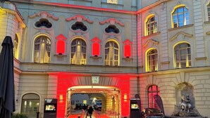Un edificio histórico con arquitectura ornamentada, una entrada iluminada con luz roja y una estatua en el patio.