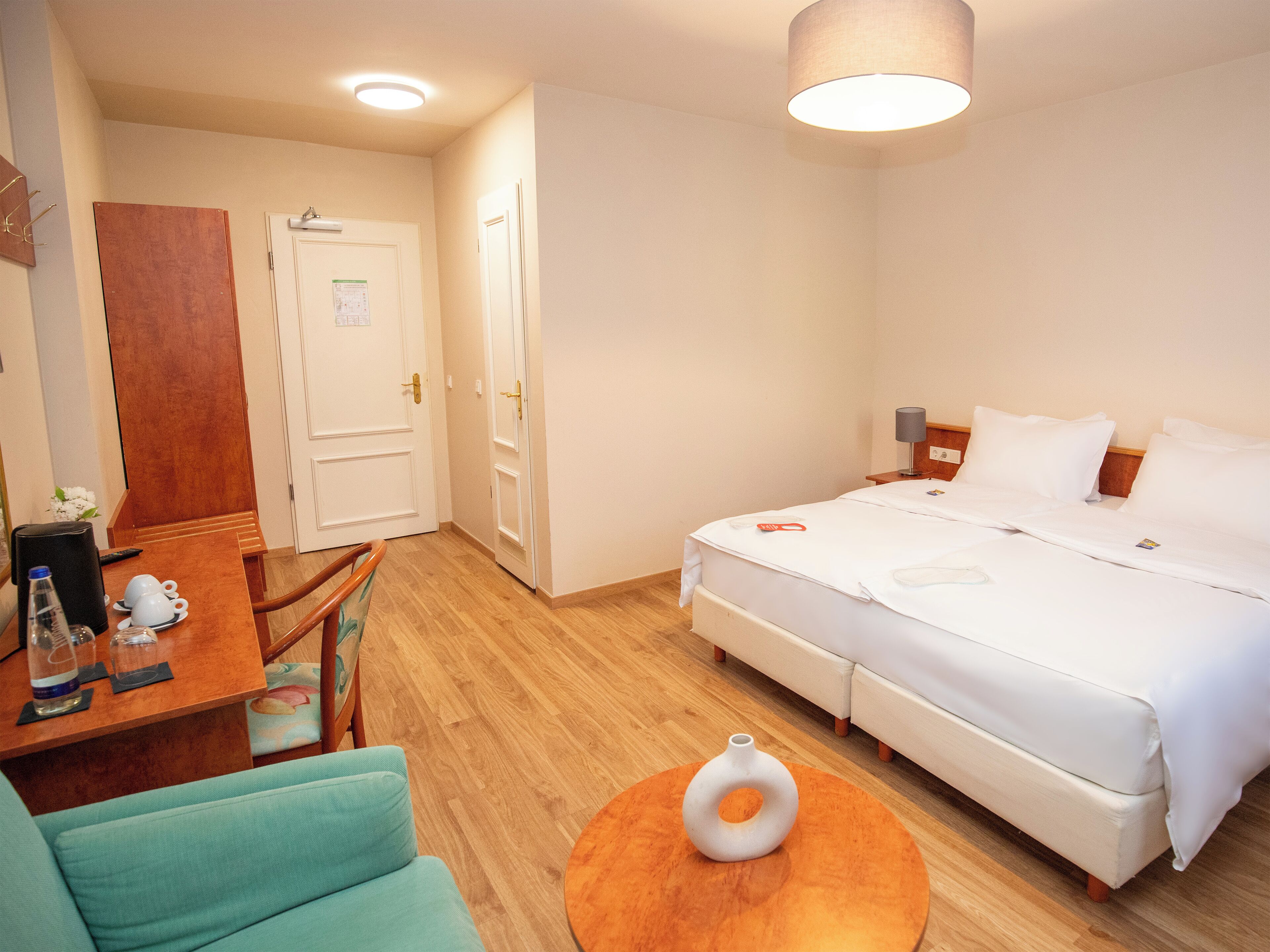 Une chambre d’hôtel avec un lit, un bureau et une chaise, une table ronde orange et un vase blanc.