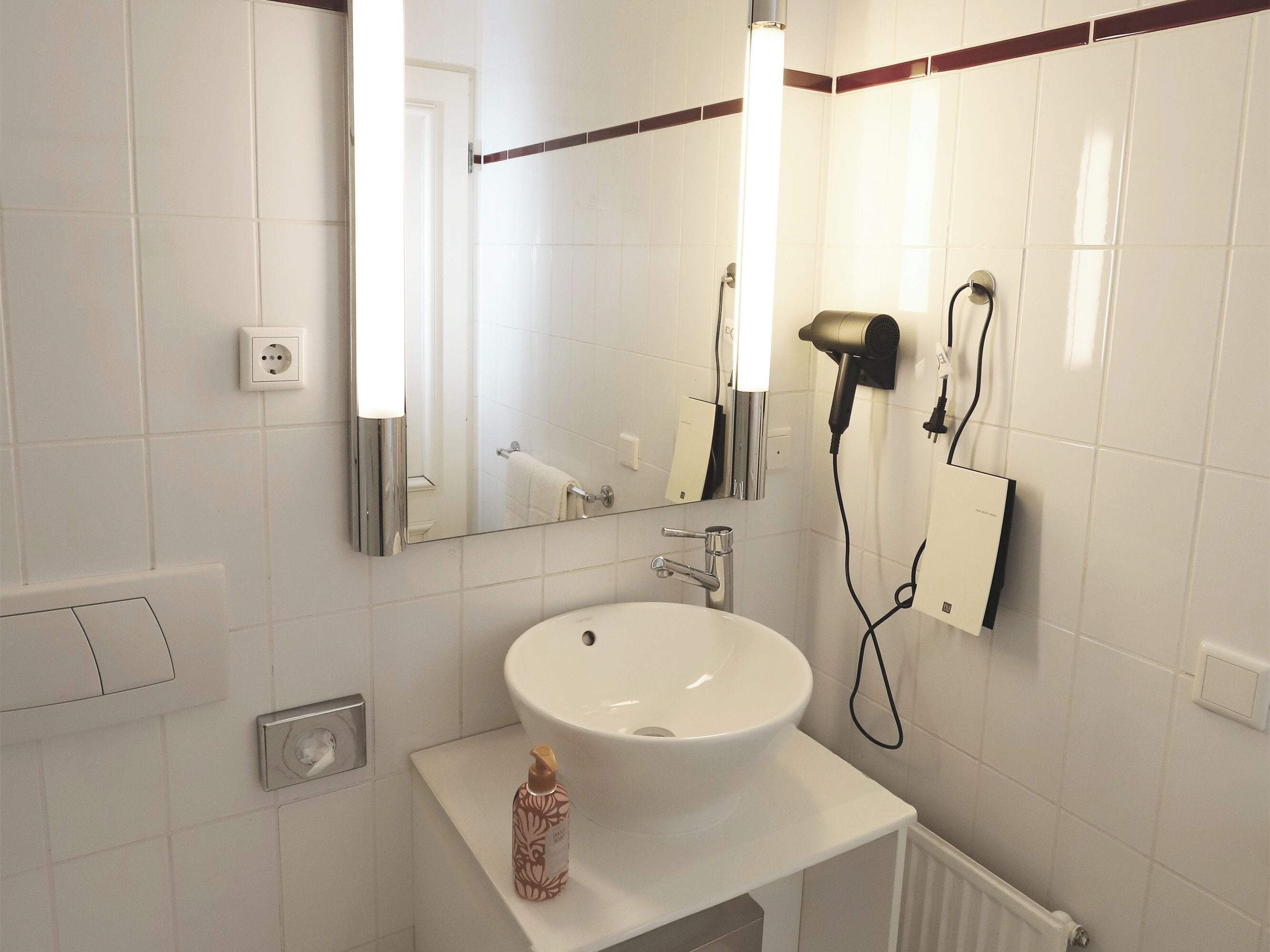 A modern bathroom with a white sink, a mirror, a hairdryer, and a towel rack.