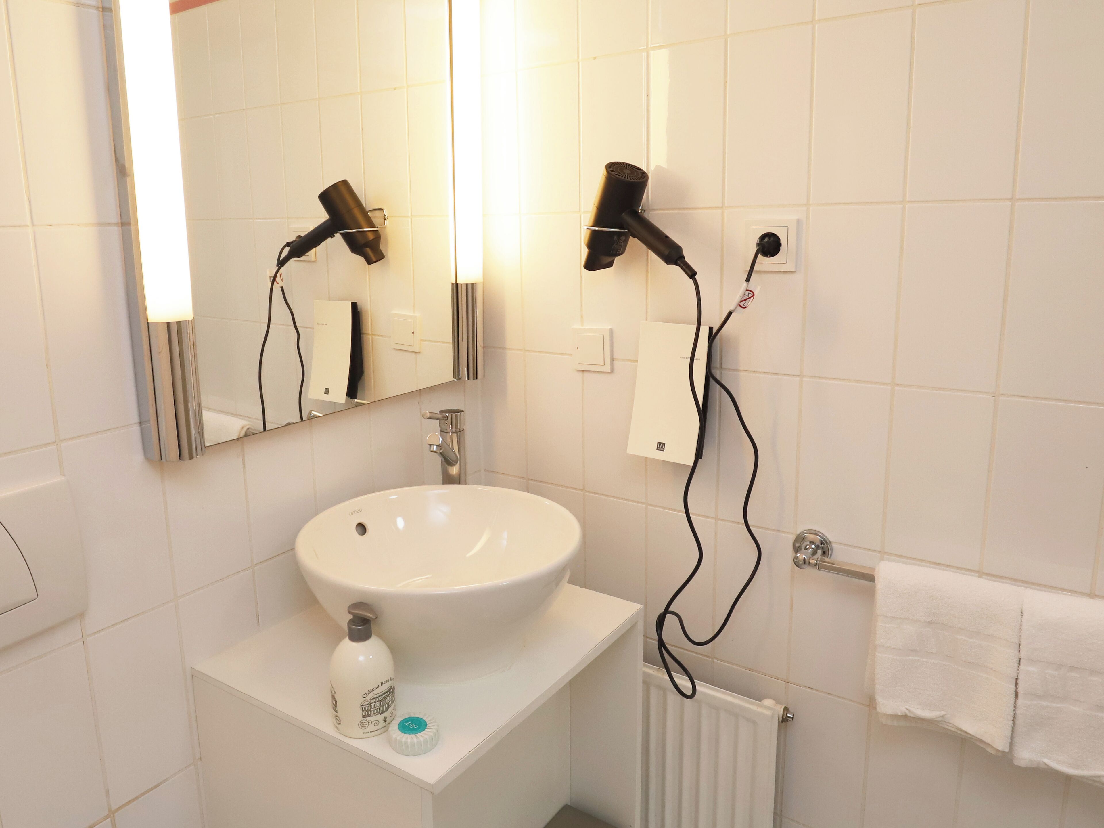 A bathroom with a white sink, a mirror, a hairdryer, and a towel rack.