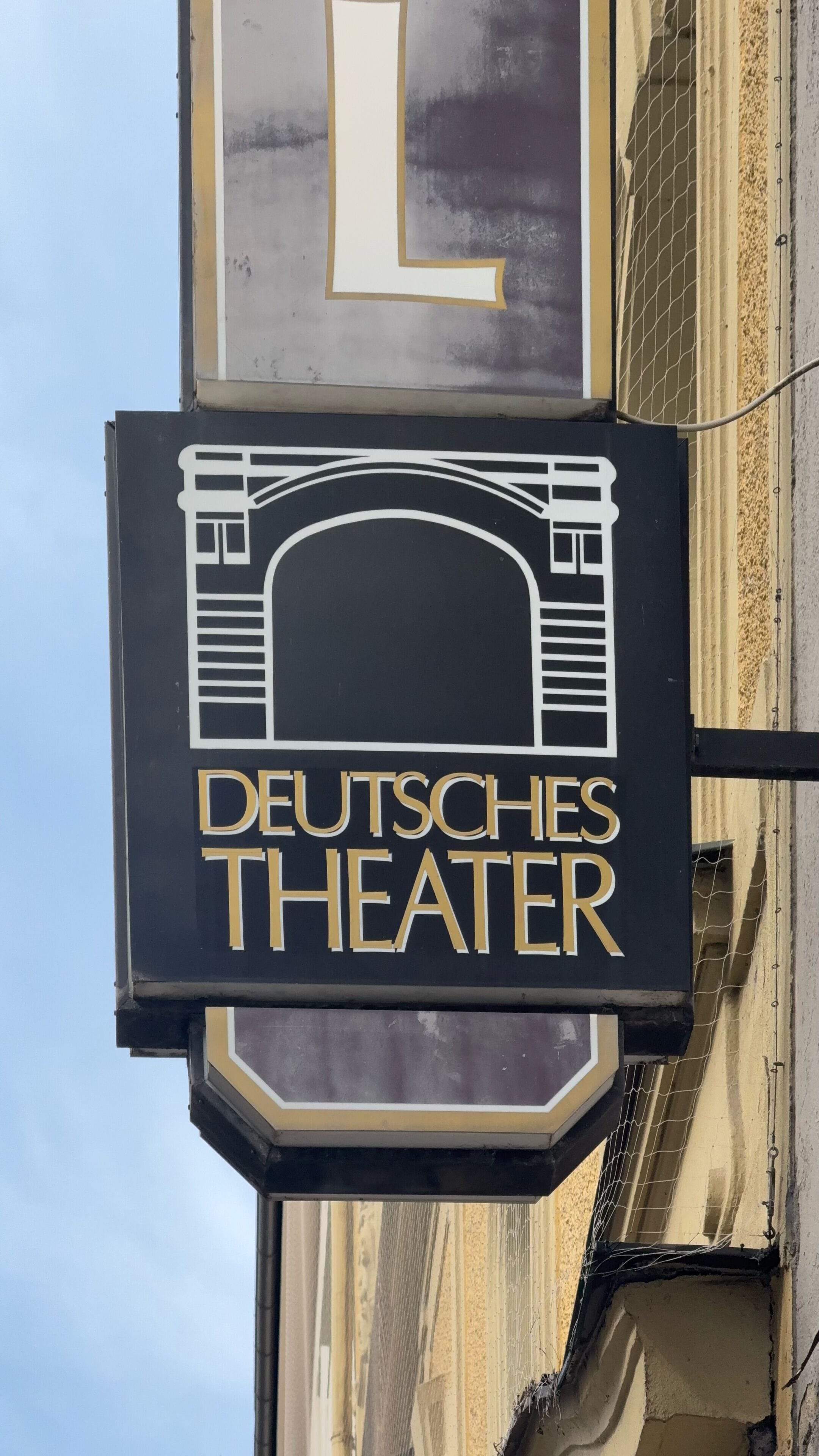 A sign for Deutsches Theater with a classical architectural design.