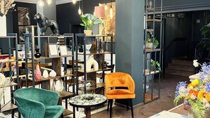 Un interior moderno con un sillón verde azulado, un sillón naranja y una vitrina de cristal con diversos objetos.