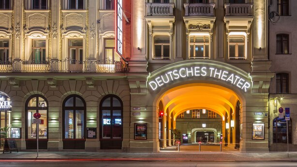 La entrada del Deutsches Theater, con una fachada ornamentada y un gran cartel iluminado.