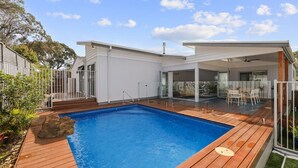 A modern house with a swimming pool, wooden deck, and glass doors leading to a patio area.