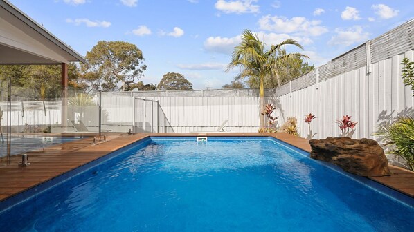 A rectangular swimming pool with a wooden deck, surrounded by a white fence and various plants. - The Palm House in Cowes (Cowes)