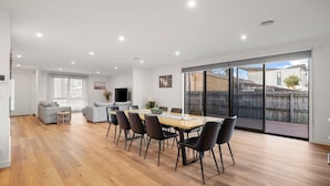 Un amplio salón con una mesa de comedor, sillas y un sofá. Cuenta con un gran ventanal corredero que da a un jardín trasero.