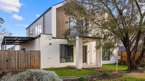 Una casa moderna de dos pisos con techo plano, ventanas grandes y cerca de madera.