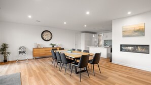 Un comedor moderno con una mesa de madera, sillas negras, un reloj y una cocina minimalista al fondo.