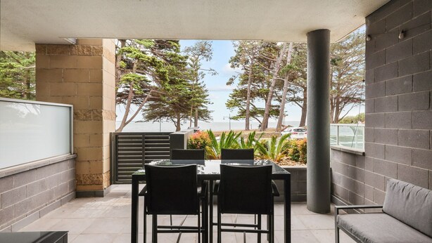 Un portico coperto con tavolo e sedie, un divano e vista sul mare e sugli alberi.