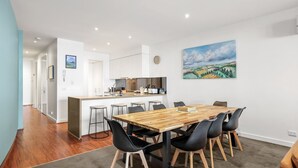Una cucina moderna con mobili bianchi, un'isola centrale con sgabelli da bar e una zona pranzo con tavolo in legno e sedie nere.