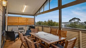 Ein überdachter Sitzbereich im Freien mit Holztisch und -stühlen, einem Grill und Blick auf die umliegende Landschaft.