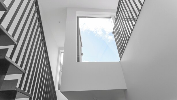 Un interior moderno con techo alto, tragaluz y escalera con barandilla a rayas.