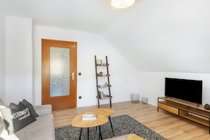 A modern living room with a sofa, a coffee table, a TV, a bookshelf, and a door.