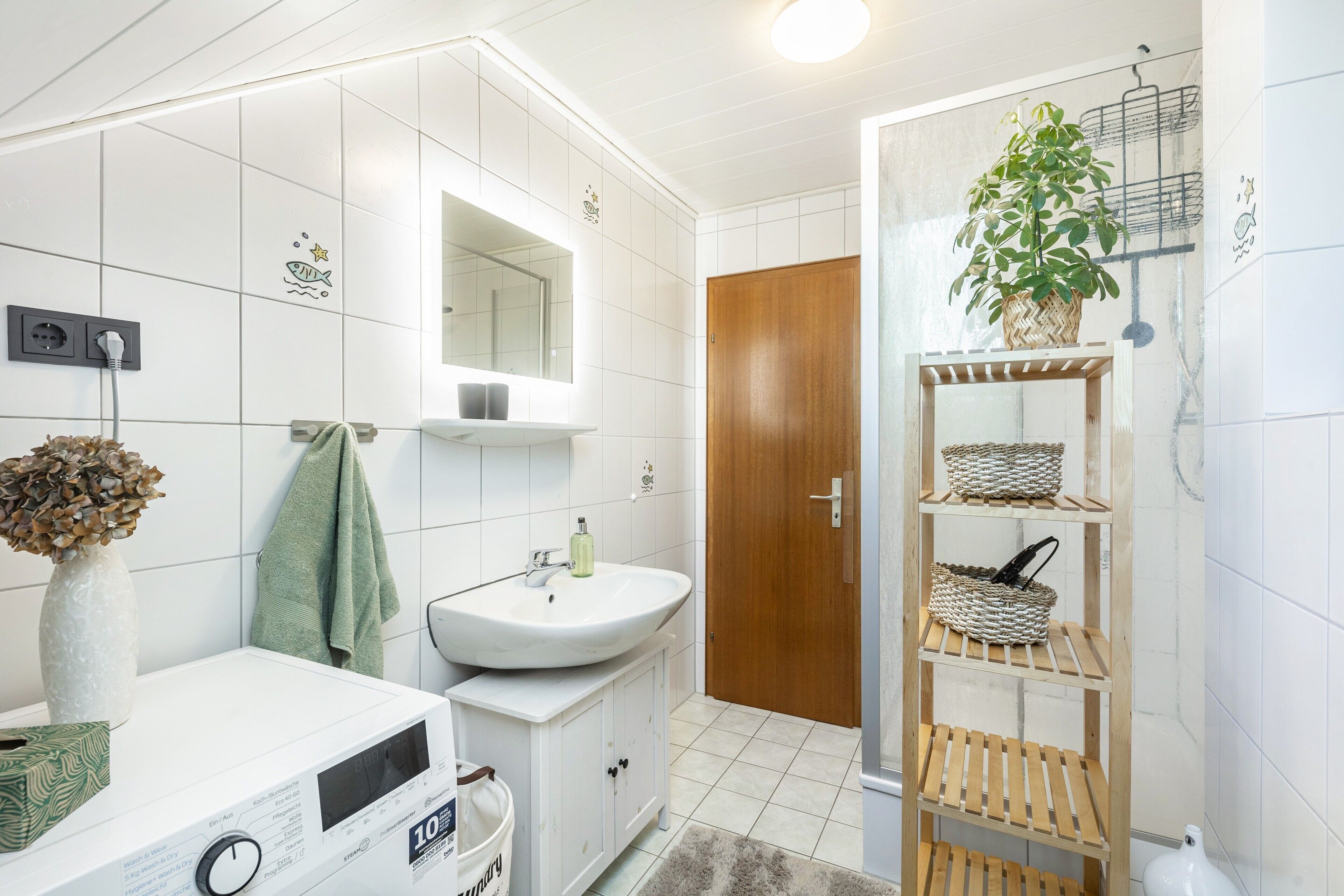 Une salle de bain avec un lavabo blanc, un miroir et une étagère en bois sur laquelle sont posés des paniers.