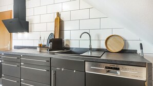 Una cocina moderna con lavavajillas negro, un fregadero y una tabla de cortar de madera sobre la encimera.