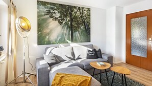 Una sala moderna con sofá, una mesa de centro, una lámpara de pie y una obra de arte de gran tamaño con temática forestal en la pared.