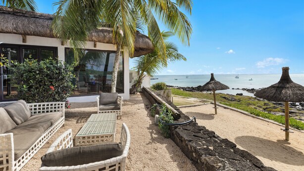A beachside patio with wicker furniture, a thatched-roof structure, and a view of the ocean.