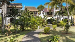 A resort with a paved walkway, palm trees, and buildings with thatched roofs.