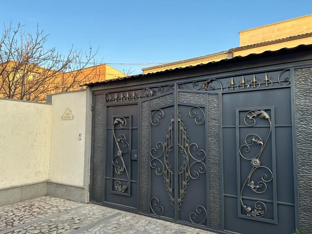 Ein schmiedeeisernes Tor mit aufwendigen Verzierungen, ein gefliestes Podest und ein Gebäude im Hintergrund.