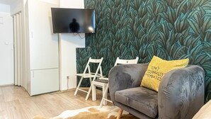 A living room with a grey sofa, a yellow pillow, a TV mounted on the wall, and a patterned wallpaper. - Comfy Hotel room | Mariahilfer Str (Vienna)