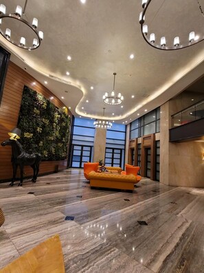 A spacious lobby with a modern chandelier, a plush orange sofa, and a decorative horse statue. - Incredible Makati Studio Unit/Stunning view &70"TV (Makati)