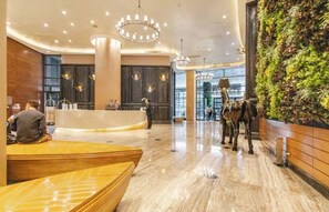 A modern hotel lobby with a reception desk, a large green wall with plants, and a marble floor.