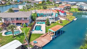 Et boligområde med et stort hus, swimmingpool, en badebro og udsigt til vandet.