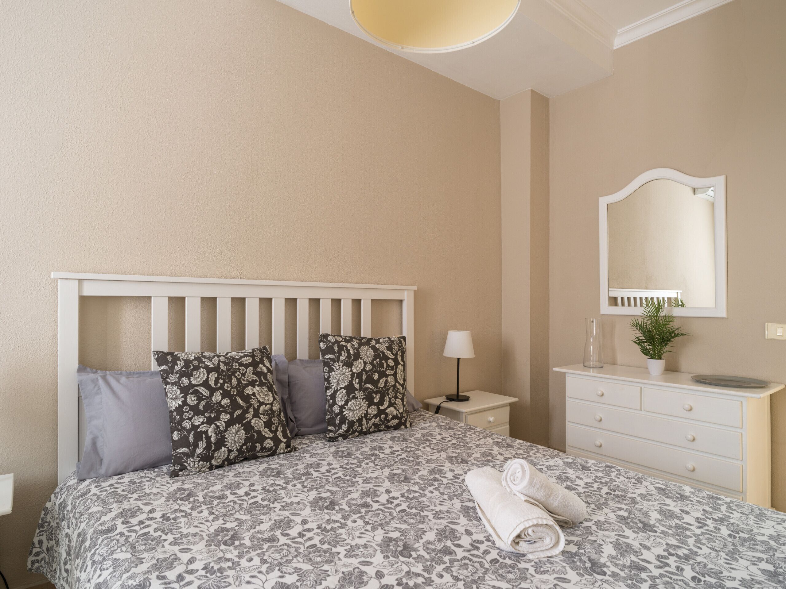 A bedroom with a bed, a nightstand, a dresser, a mirror, and a lamp.