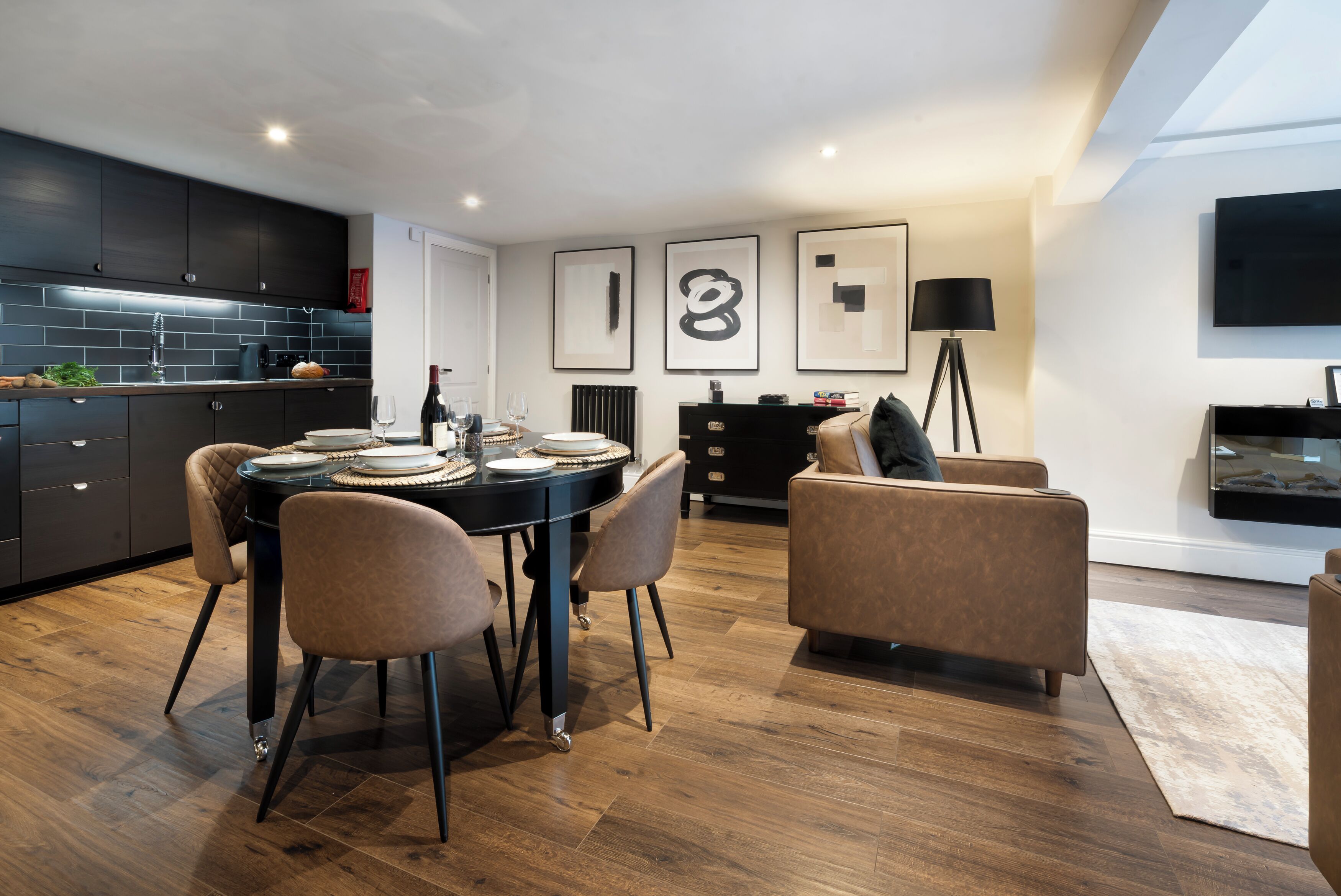 Una cocina moderna con armarios oscuros, una mesa de comedor con sillas y una sala de estar con sofá y lámpara.