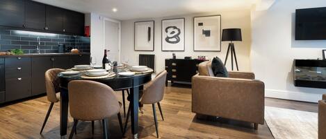 Una cocina moderna con armarios oscuros, una mesa de comedor con sillas y una sala de estar con sofá y lámpara.