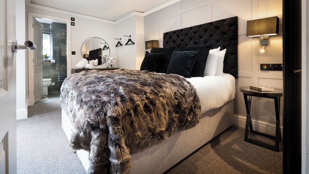 A modern bedroom with a tufted headboard, a fluffy throw blanket, and a bedside table with a lamp. - Courtyard Apartments (Bowness-on-Windermere)