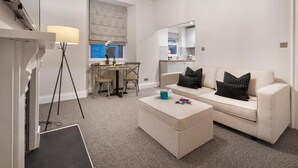 A modern living room with a sofa, coffee table, and a dining area with chairs and a table. - Courtyard Apartments (Bowness-on-Windermere)