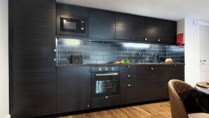A modern kitchen with dark cabinetry, a microwave, an oven, and a sink. - Courtyard Apartments (Bowness-on-Windermere)