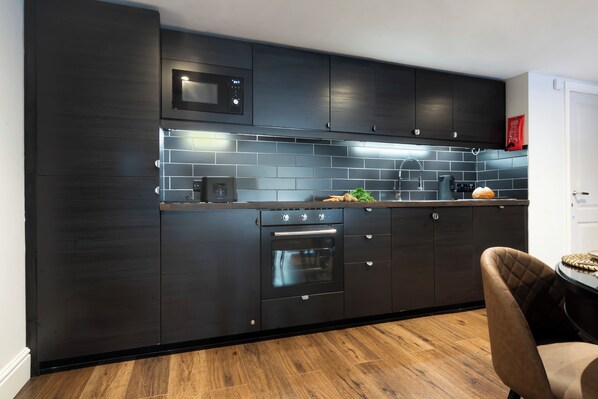 Una cocina moderna con armarios oscuros, un microondas, un horno y un lavamanos.
