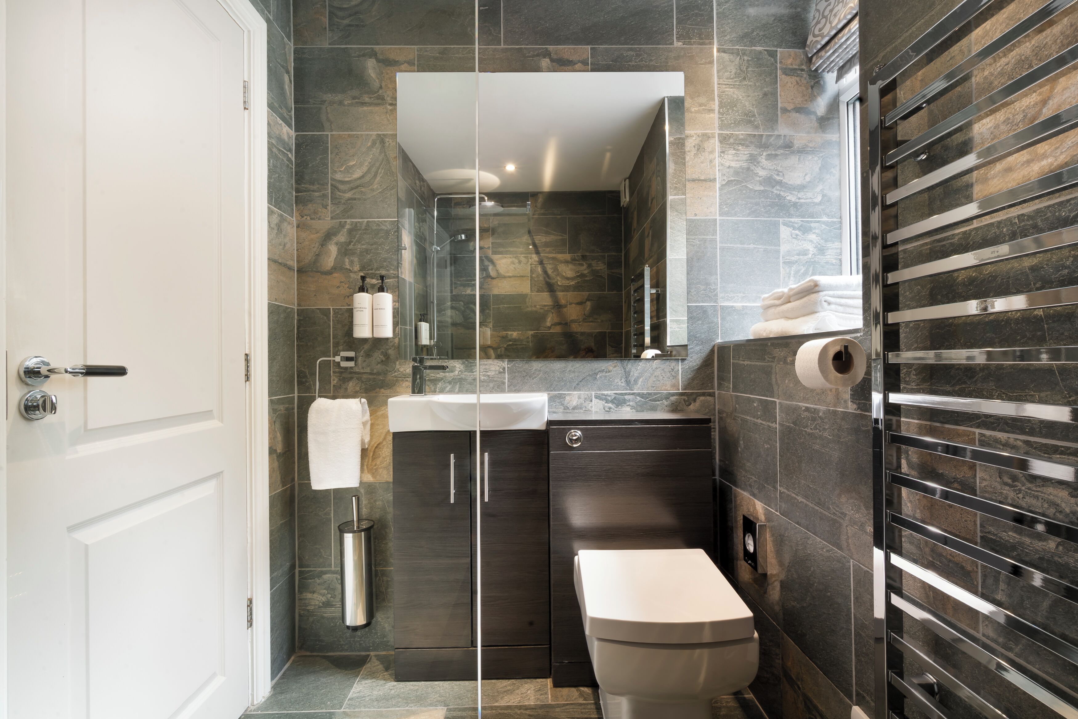 Un baño moderno con cabina de ducha de vidrio, tocador de madera oscura y váter blanco.