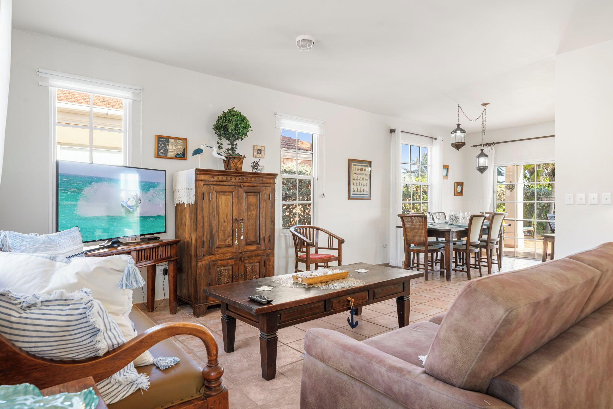 A spacious living room with a large flat-screen TV, wooden furniture, and a dining area with chairs and a table.