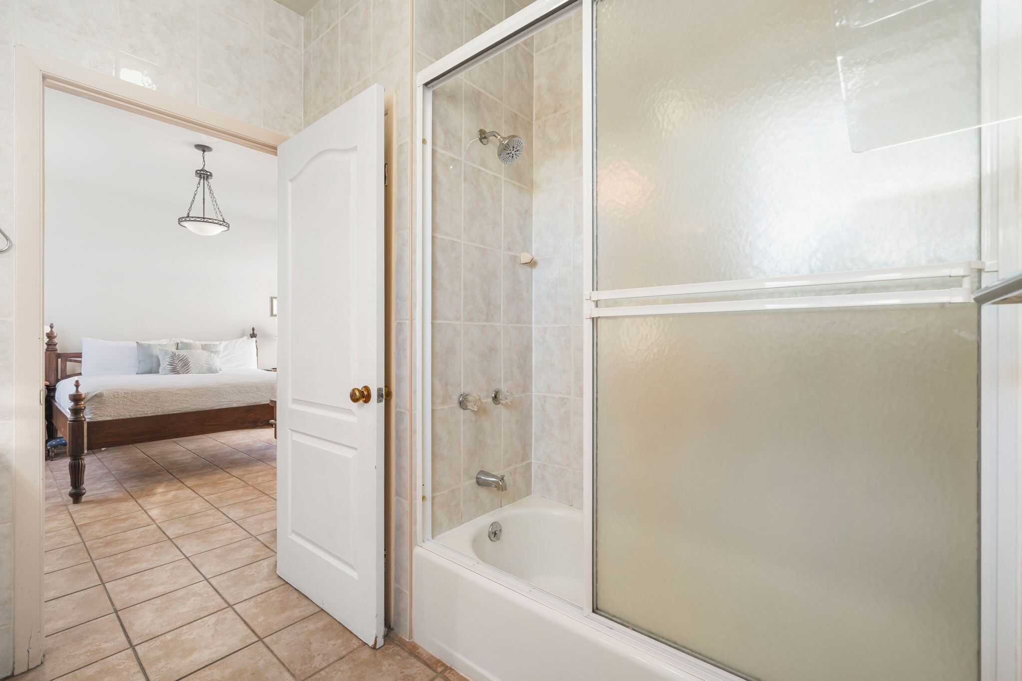 A bathroom with a bathtub, a shower enclosure, and a bed with a nightstand.
