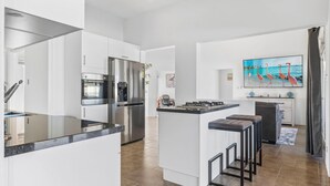 Een moderne keuken met een centraal eiland, roestvrijstalen apparatuur en een groot raam met een schilderij van flamingo's.